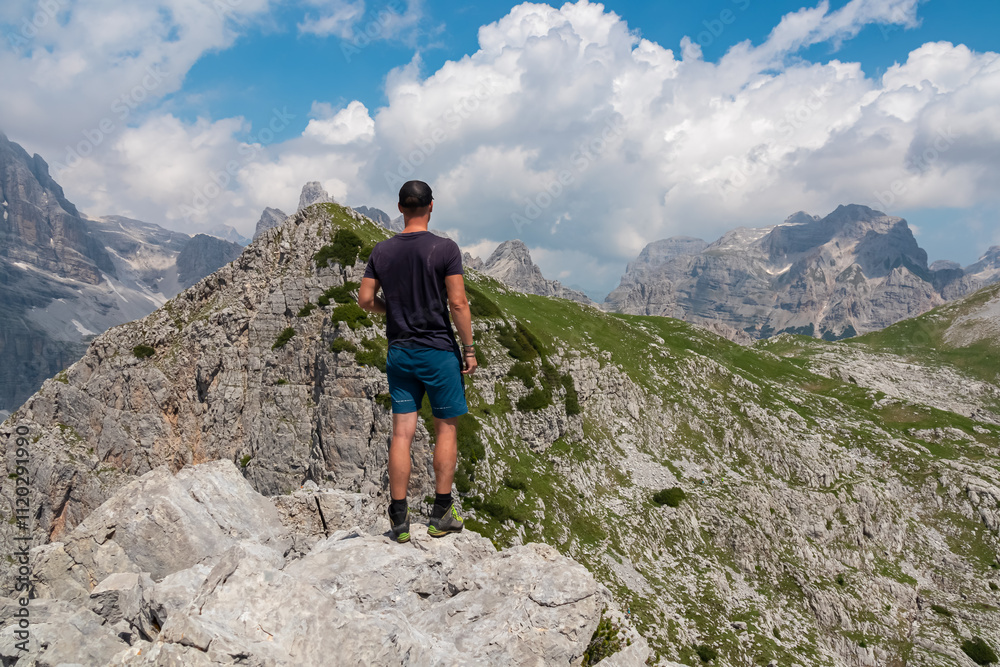 Hiker man on top of Croz dell'Altissimo with panoramic view of majestic cloud covered rugged mountain peaks of Brenta Dolomites, Trentino, Italy. Summer wanderlust in alpine wilderness Italian Alps Hiker man on top of Croz dell'Altissimo with panoramic view of majestic cloud covered rugged mountain peaks of Brenta Dolomites, Trentino, Italy. Summer wanderlust in alpine wilderness Italian Alps