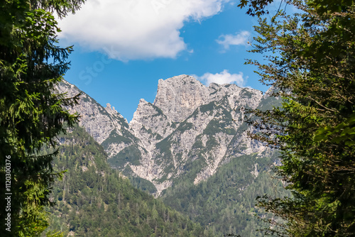 Lush green forest framing scenic view of pristine rugged mountain peaks of Western Julian Alps, Italy, Europe. Wild hiking trail, Triglav National Park. Wanderlust in alpine wilderness in summer photo