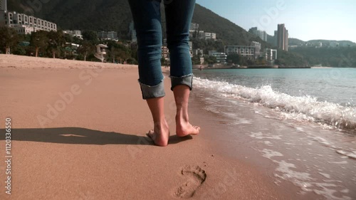 Legs of a beautiful young woman in jeans walking along the Hong Kong beach in sunshine