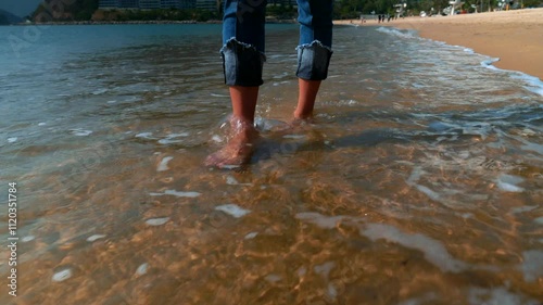 Feet of a beautiful young sporty woman in jeans walking in the water along the Hong Kong beach in sunshine