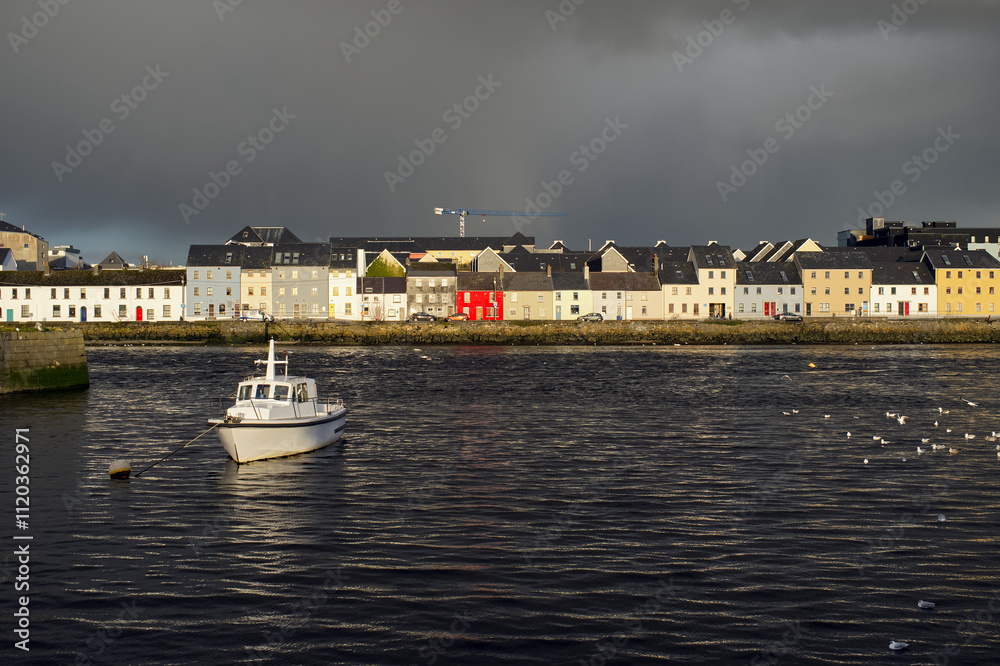 Beautiful cityscape sunrise scenery with old wooden boat in Corrib river at Claddagh in Galway city, Ireland, architecture background