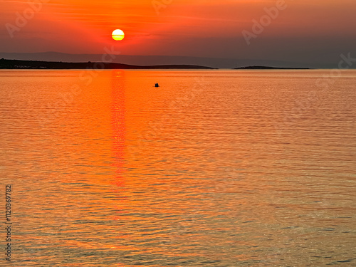 Breathtaking fiery sunset over calm Adriatic Mediterranean Sea in Premantura, Istria peninsula, Croatia, Europe. Reflection of the sun on water creates shimmering path that extends towards horizon photo