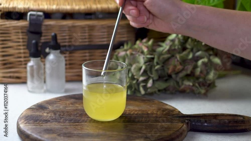 Mixing liquid ingredients in a glass when making a natural cosmetic on dark wood background. 