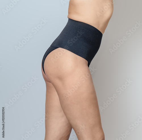 Naked female body in black postpartum panties on gray background. Body positive concept, Side view. photo