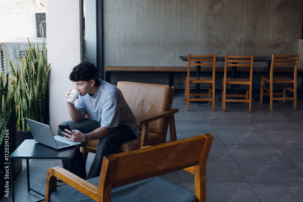 Entrepreneur man looking at phone while drinking coffee and working on laptop in cafe Entrepreneur man looking at phone while drinking coffee and working on laptop in cafe