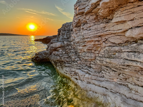 Rock formation with layered texture in sunrise scene at remote beach in Kamenjak National Park. Warm golden glow on cliffs by Adriatic Mediterranean Sea in Premantura, Istria peninsula, Croatia photo