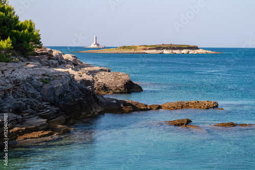 Scenic view of white lighthouse Porer seen from the rocky shoreline of Cape Kamenjak National Park near Premantura, Istria, Croatia. Calm water of the Adriatic Mediterranean Sea in summer. Seascape photo