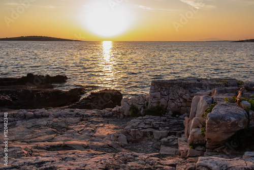 Fototapeta Naklejka Na Ścianę i Meble -  Romantic sunrise scene at remote stone beach in Kamenjak National Park. Warm golden glow on cliffs by Adriatic Mediterranean Sea in Premantura, Istria peninsula, Croatia. Islands in the distance