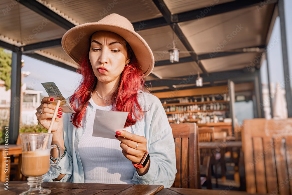 Young woman sitting at a restaurant table with a displeased expression checking the bill and paying in cash