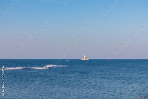 Jetskis surrounding white lighthouse Porer build on small islet seen from Cape Kamenjak National Park near Premantura, Istria, Croatia. Calm water of the Adriatic Mediterranean Sea in summer. Seascape photo