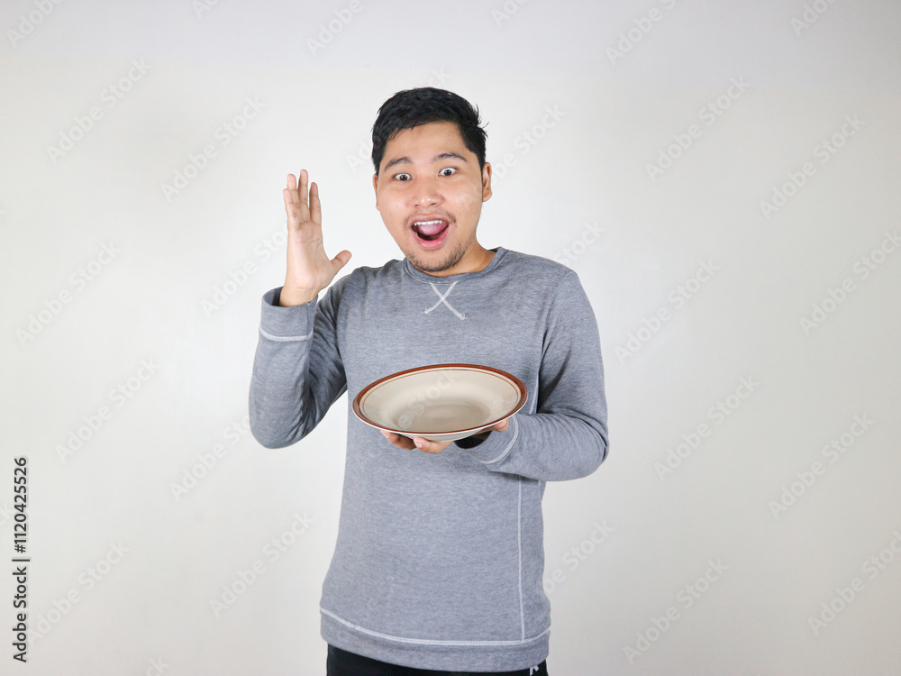 Asian man holding an empty plate and looking at the plate he was holding with a shocked expression Asian man holding an empty plate and looking at the plate he was holding with a shocked expression