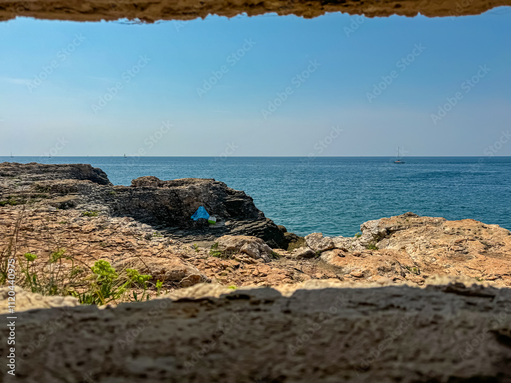 Bunker window framing view of rugged coastal landscape with rocky cliffs in Adriatic Mediterranean Sea. Travel destination Banjole on Istria peninsula, Kvarner Gulf, Croatia, Europe. Summer vacation Bunker window framing view of rugged coastal landscape with rocky cliffs in Adriatic Mediterranean Sea. Travel destination Banjole on Istria peninsula, Kvarner Gulf, Croatia, Europe. Summer vacation
