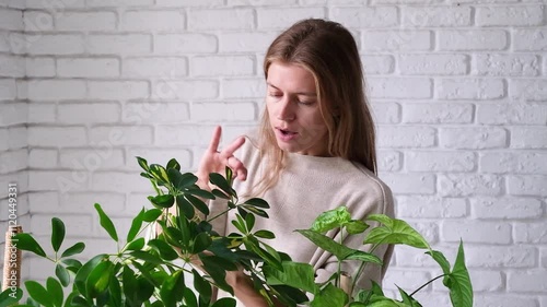 young Caucasian millennial woman caring about plants at home doing her daily routine, white brick wall background