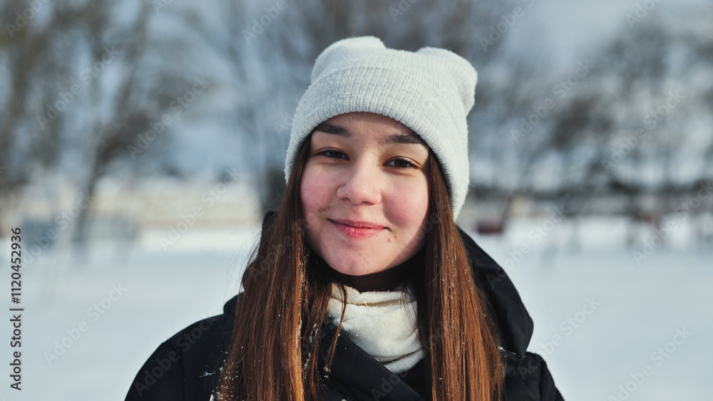 Young schoolgirl wearing winter clothes and smiling during a snowy park photoshoot Young schoolgirl wearing winter clothes and smiling during a snowy park photoshoot