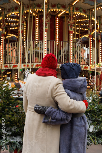 Back of senior friends in outdoor Christmas market holidays. Diversity, happy and elderly people in retirement at illuminated carnival Christmas carousel