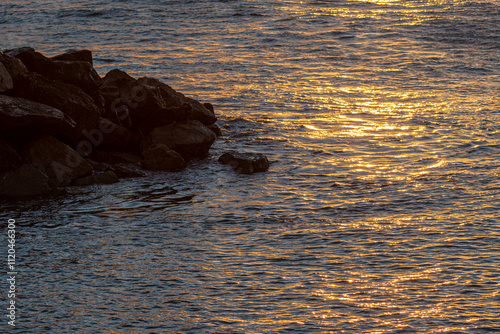 Rocas en el mar al atardecer, con reflejos dorados en el agua. photo