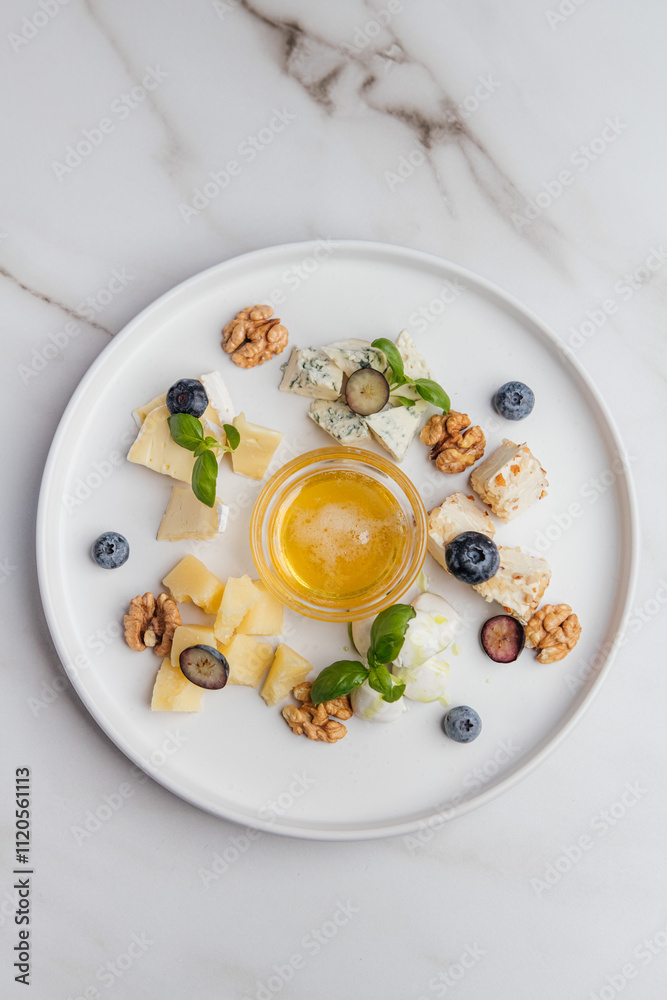 Round white plate with assorted cheese, honey, blueberries, walnuts and basil leaves, arranged in a beautiful composition, creating food presentation. Restaurant or cafe menu, cookbook recipe
Round white plate with assorted cheese, honey, blueberries, walnuts and basil leaves, arranged in a beautiful composition, creating food presentation. Restaurant or cafe menu, cookbook recipe