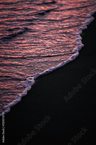 The gentle waves leave a trail of foam on the darkened sand, reflecting the vibrant hues of pink and orange from the setting sun. photo