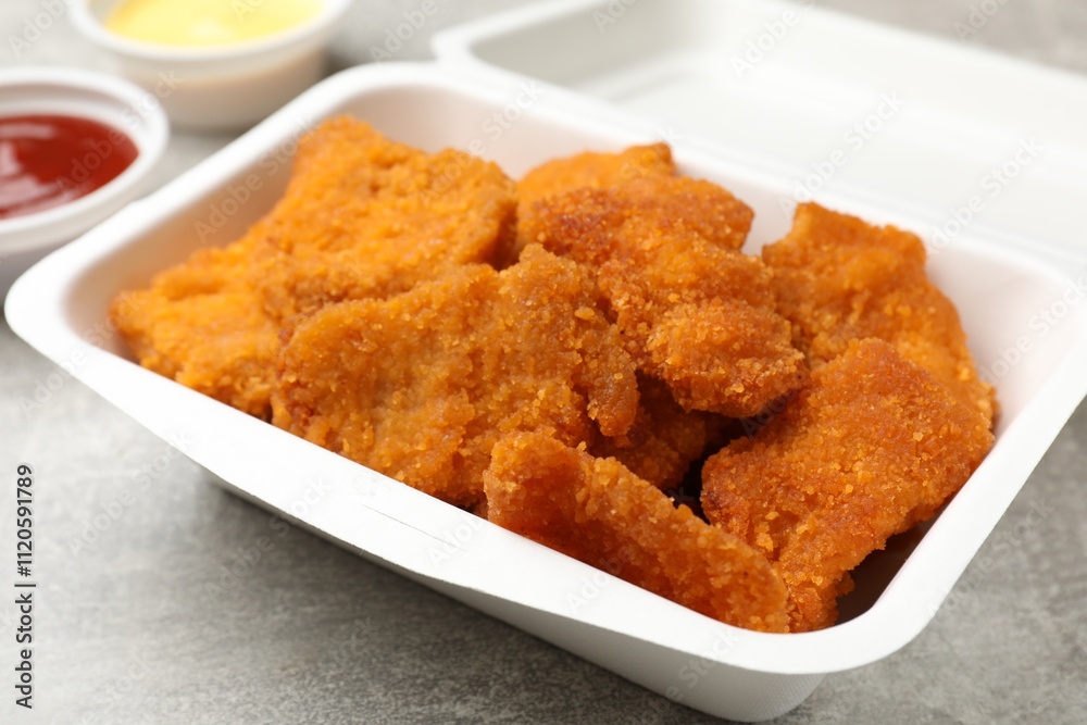 Delicious chicken nuggets in takeaway container on grey textured table, closeup Delicious chicken nuggets in takeaway container on grey textured table, closeup