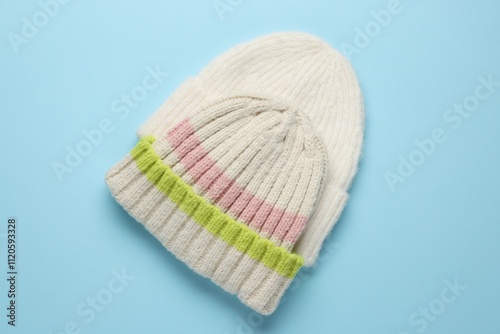 Warm woolen hats on light blue background, top view