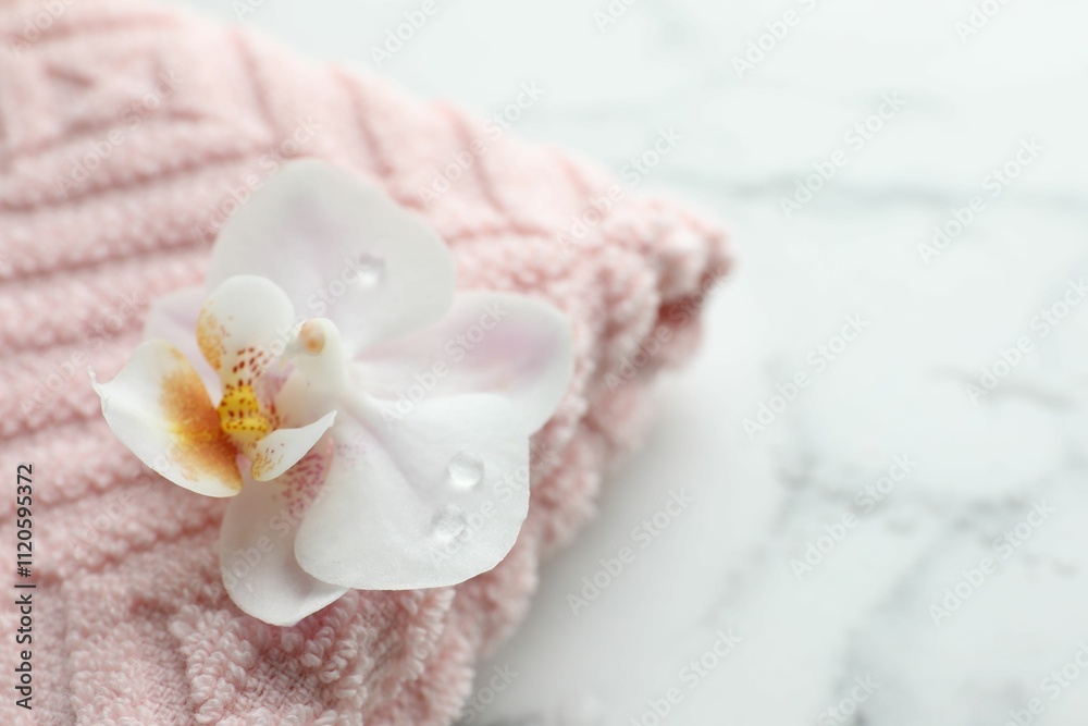 Orchid flower and towel on white marble table, closeup. Space for text Orchid flower and towel on white marble table, closeup. Space for text
