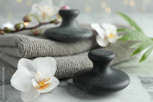 Spa stones, orchid flowers, towels and palm leaf on white marble table, closeup photo