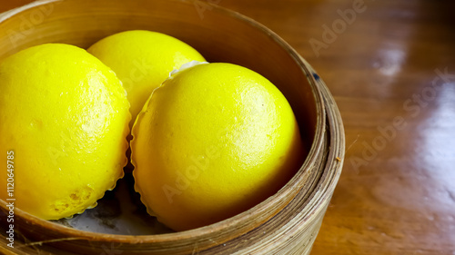 Three golden-yellow baozi chinese steamed buns arranged in a bamboo steamer basket, placed on a wooden table, exuding a warm and appetizing appearance