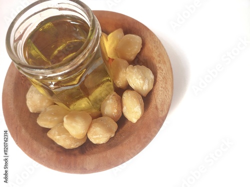 A clean jar filled Candlenuts essential oil with Dried Indonesian Candlenuts on wooden plate, or Kemiri in Indonesia, the seed of Aleurites moluccanus isolated on the white background. Copy space photo