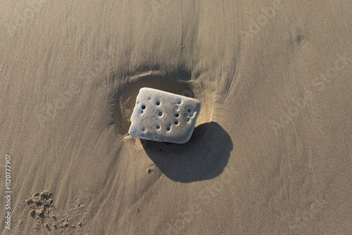 Cubic rock with holes in the sand on the beach