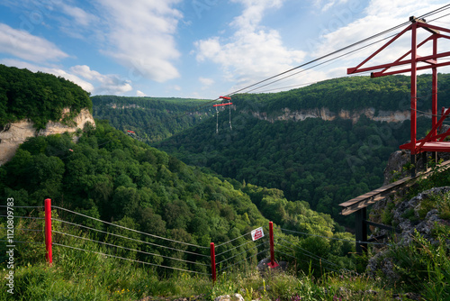 Zipline attraction through the Mishoko River Canyon in the Caucasus Mountains in the Mishoko Extreme Park on a sunny summer day, Kamennomostsky village, Republic of Adygea, Russia photo