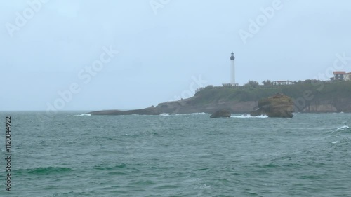 Stormy ocean waves under the rain and lighthouse of Biarritz in the background