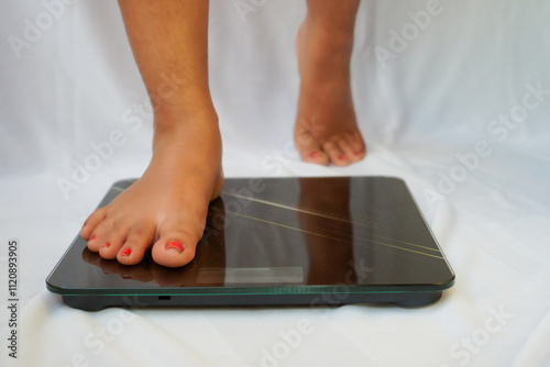 A young woman barefoot and stepping on floor scales. Woman feet standing weighing scales, slimming. Weight loss scales measure weight. Health and wellness.