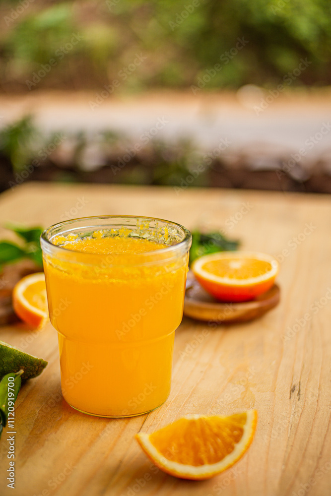 A glass of freshly squeezed orange juice on a wooden table surrounded by orange slices and orange leaves A glass of freshly squeezed orange juice on a wooden table surrounded by orange slices and orange leaves