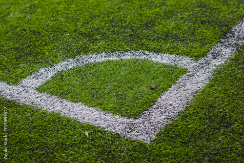 close-up view of a section of a sports field, specifically a corner area. The field is covered in green artificial turf with white painted lines marking the boundaries.