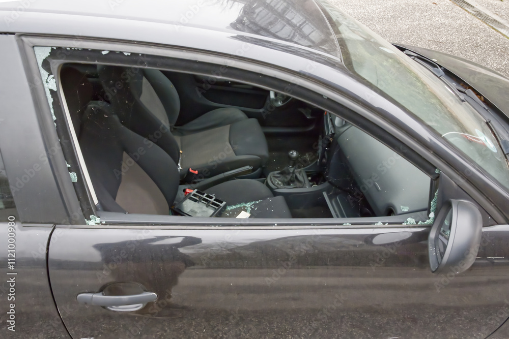 Fototapeta premium The window of the passenger door of a black car was smashed in order to steal the radio and other valuables, shards and remains of the tempered safety glass remained in the window frame