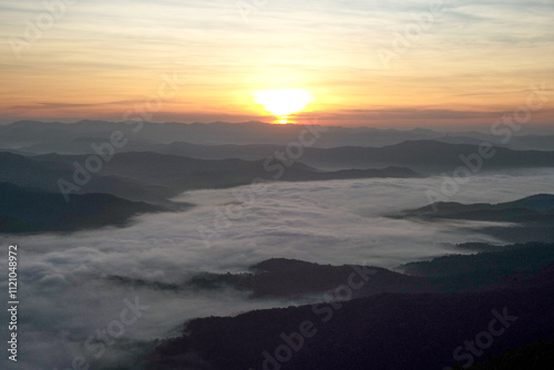 Panorama view layers of mountain with the fluffy white fog between the mountains and orange sunrise sky in background