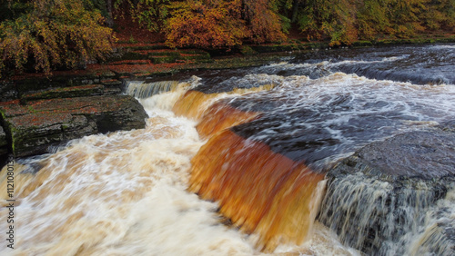 Aerial view of large volume of water passing over waterfall in Autumnal woodland  photo