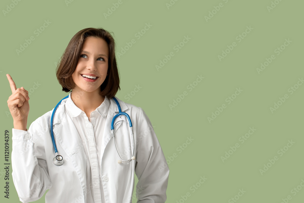Beautiful female doctor with stethoscope pointing at something on green background Beautiful female doctor with stethoscope pointing at something on green background