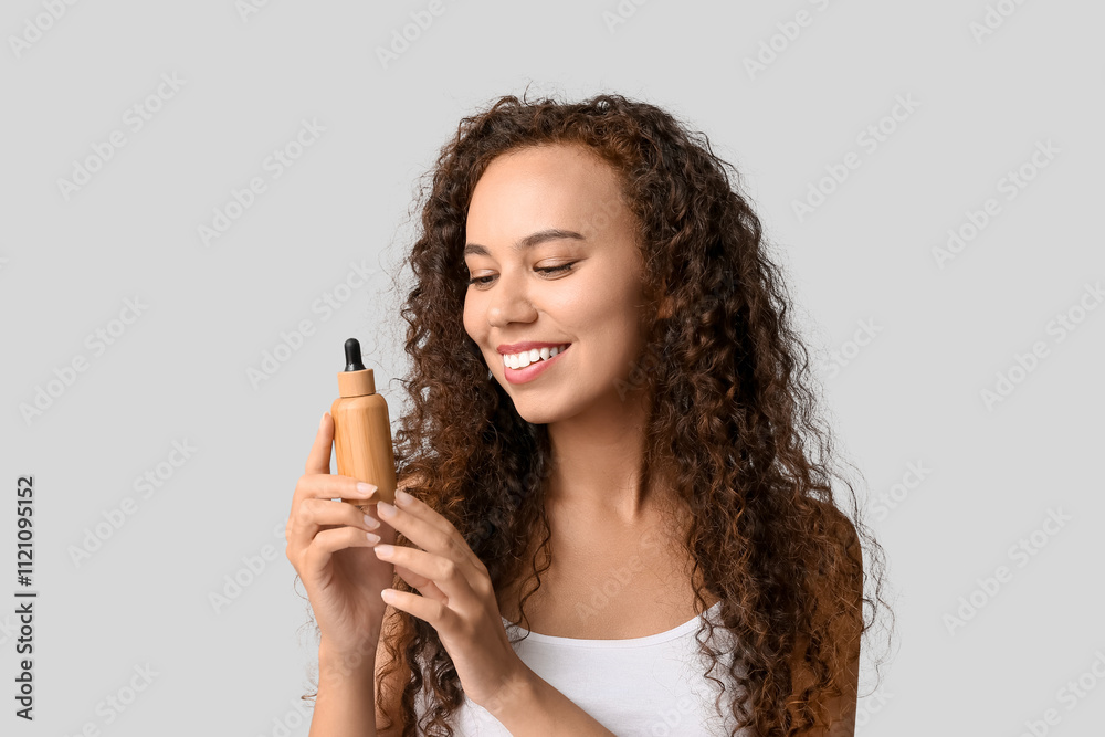 Beautiful young African-American woman with bottle of face serum on white background Beautiful young African-American woman with bottle of face serum on white background