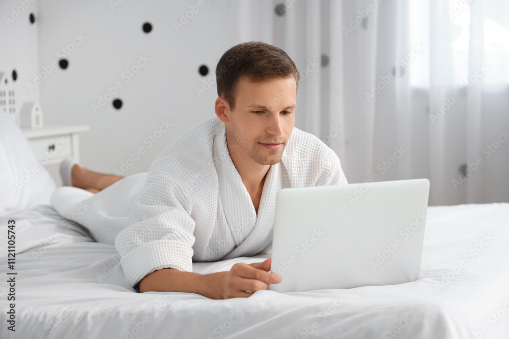 Young man in bathrobe using laptop on bed at home Young man in bathrobe using laptop on bed at home
