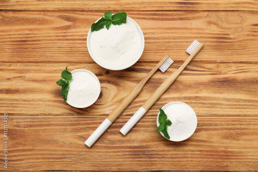 Bowls of tooth powder with mint leaves and brushes on wooden background. Top view Bowls of tooth powder with mint leaves and brushes on wooden background. Top view