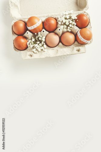 Brown Easter eggs decorated lace and white gypsophila flowers in carton on white background. Easter celebration concept. Top view photo of festive food of painted chicken egg retro toned photo