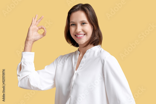 Pretty young woman showing OK on yellow background