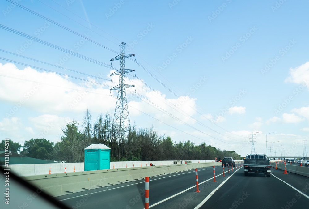 Portaloo on a blocked lane of highway for maintenance. Transmission towers and power lines along the motorway. Auckland.