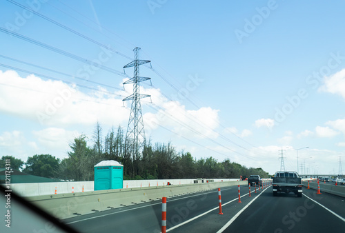 Portaloo on a blocked lane of highway for maintenance. Transmission towers and power lines along the motorway. Auckland.