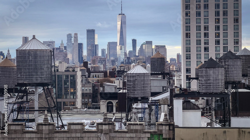 A cloudy New York City skyline featuring iconic rooftop water towers, historic architecture, and modern high-rises, capturing urban contrast