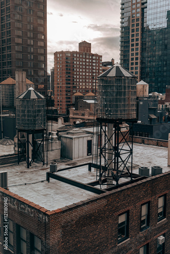 A cloudy New York City skyline featuring iconic rooftop water towers, historic architecture, and modern high-rises, capturing urban contrast