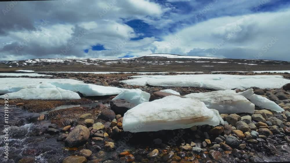 Small water stream in gravel ground with ice pieces in a desert with snowy terrain in the background Small water stream in gravel ground with ice pieces in a desert with snowy terrain in the background