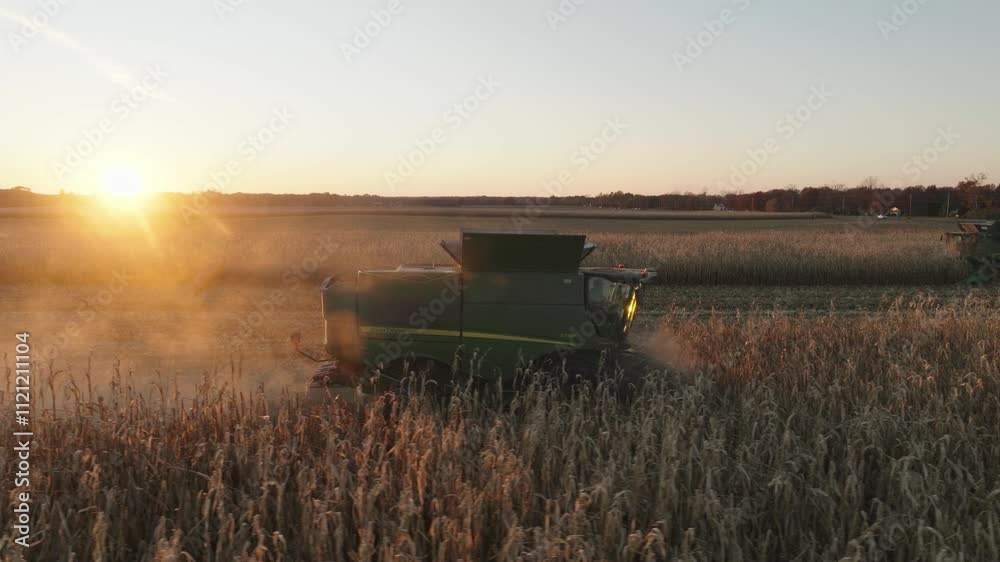 Aerial footage of a combine harvesting corn in a vast rural field during sunset, with warm golden hues and visible farming equipment in action.