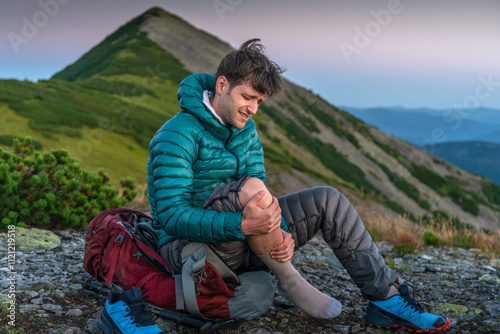 Man is Traveling with Backpack and has Problems with Sprained Ankle in the Mountains. Man with ankle injury feels pain in leg with an expression of pain on his face.